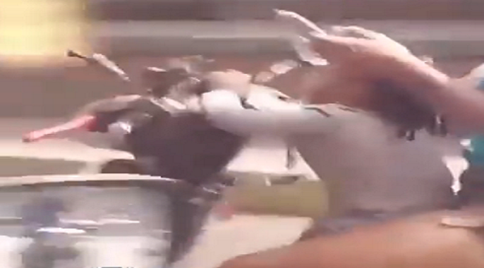 Una mujer maneja su moto por Petare con una bebé mientras revisa su teléfono